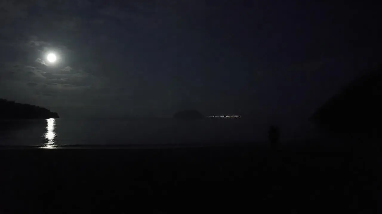 Noche tranquila, playa oscura, silueta distante